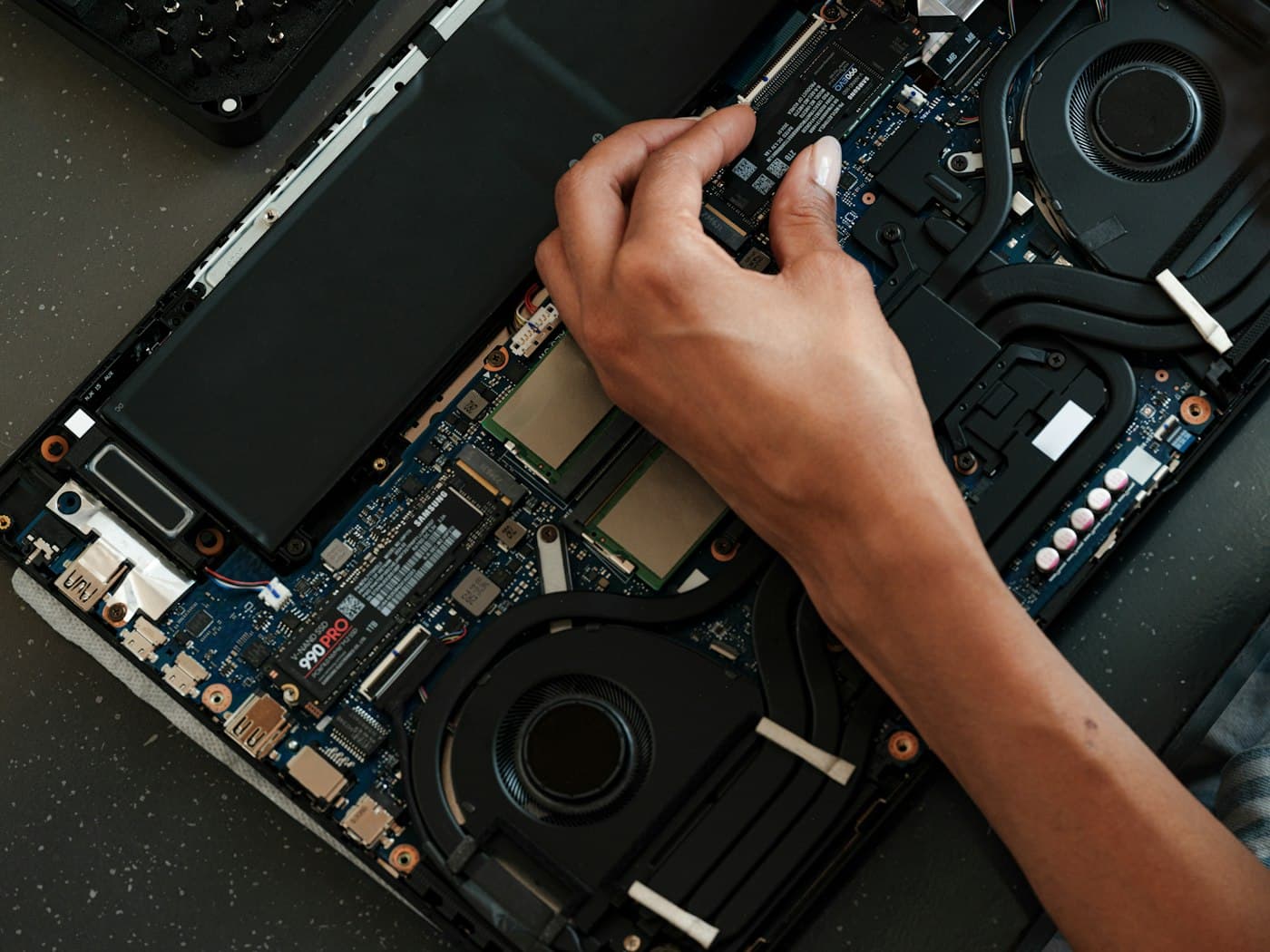 A technician fitting a solid state drive inside an opened laptop.